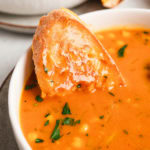 close up of grilled cheese sandwich dipped into a bowl of tomato soup with chickpeas