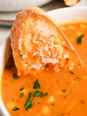 close up of grilled cheese sandwich dipped into a bowl of tomato soup with chickpeas