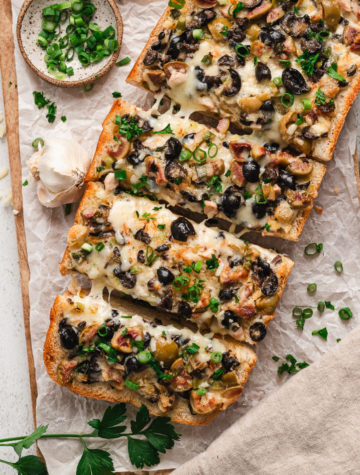 garlic bread loaf topped with melty cheese and chopped black olives and garlic olives